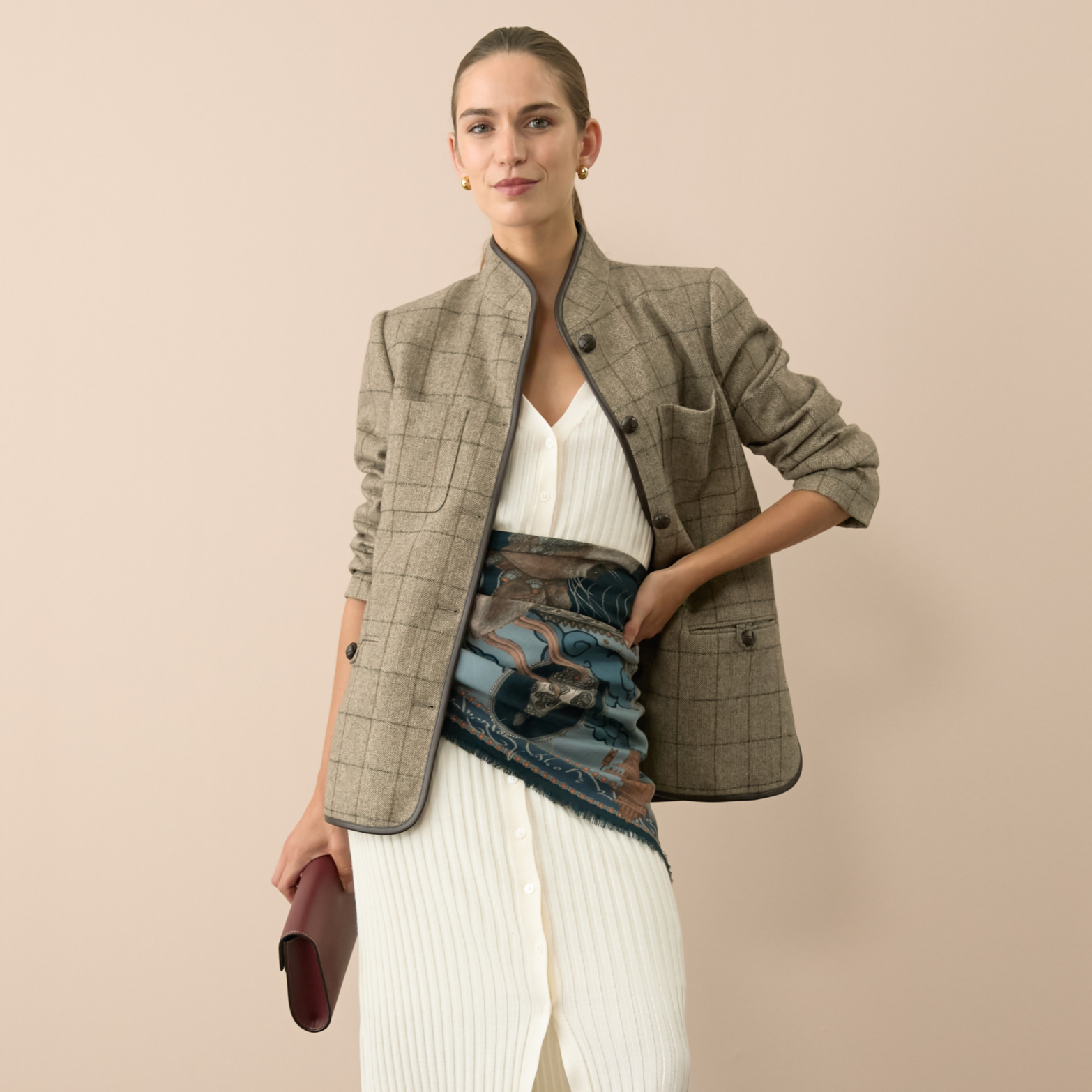 Woman in classic light brown checked blazer and white knit dress, styled with an effortless blue sash and burgundy clutch; a fun, high-end look.