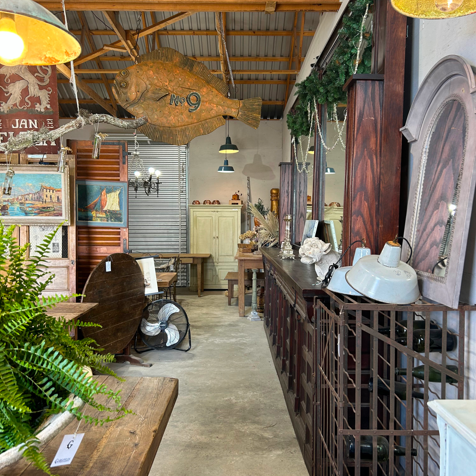Indoor antique shop with a classic copper fish sculpture, rustic tables, lush fern, and an effortless mix of vintage decor for a fun, high-end feel.