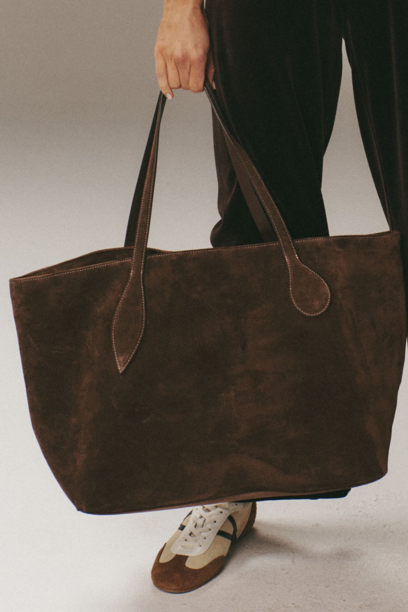 Person holding the classic Dark Brown Suede Large Sprout Tote, an effortless, high-end weekend bag with snap closure and internal pocket, embodying fun and sophistication.