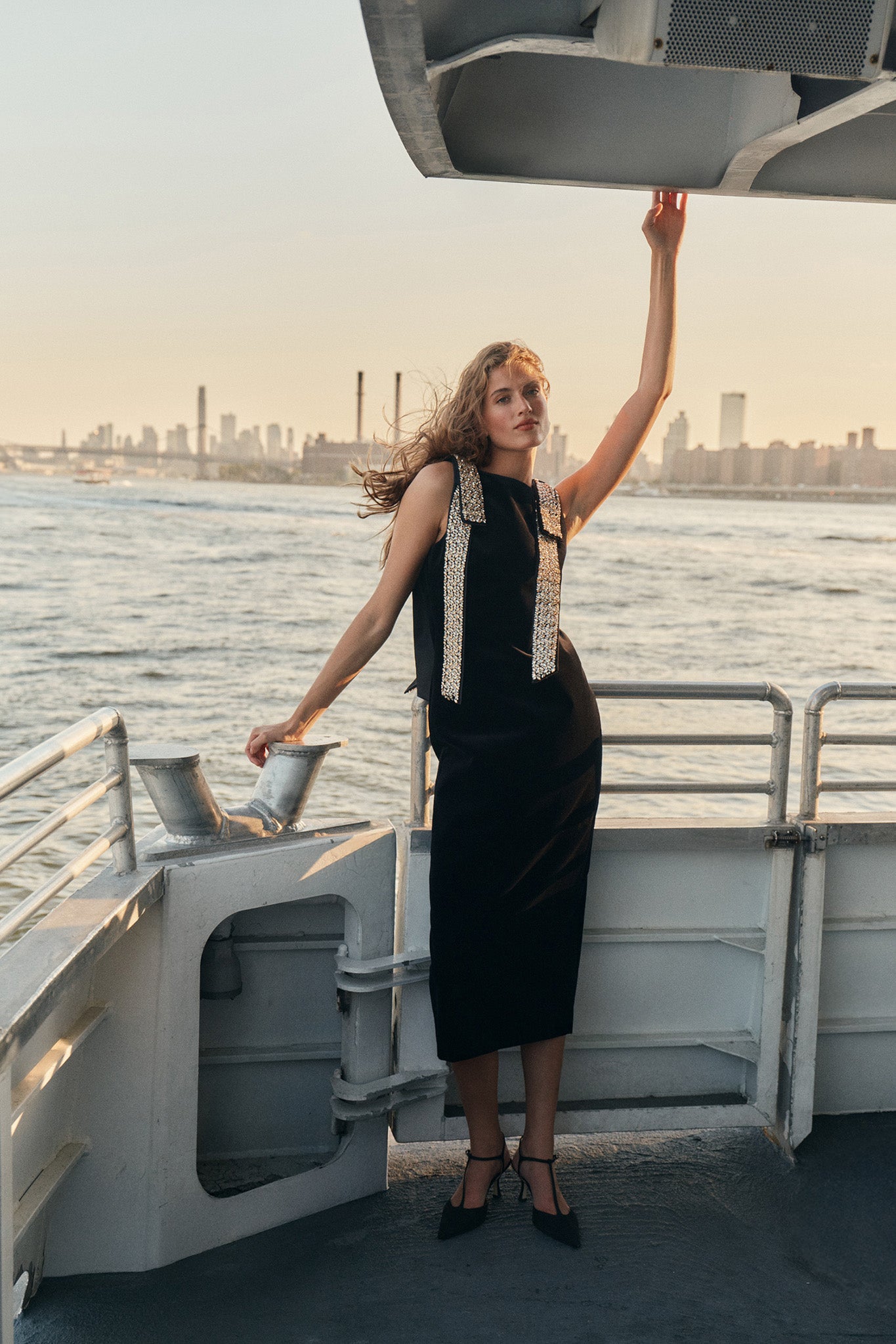 A woman on a ferry wearing a black midi dress with embellished shoulder bows and black t-strap heels.