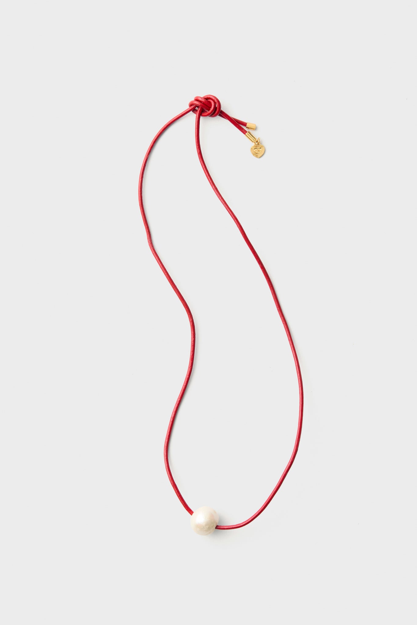 A HART red pearl cord necklace features a single white pearl bead and a small gold disc charm, elegantly displayed.