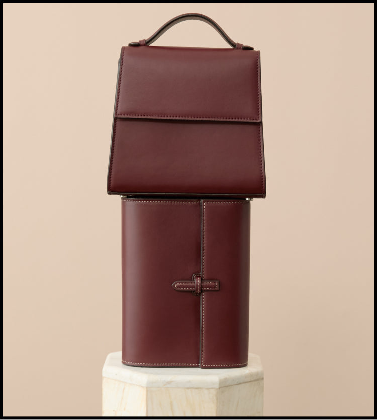Two leather bags stacked on top of each other. One has a top handle. 
