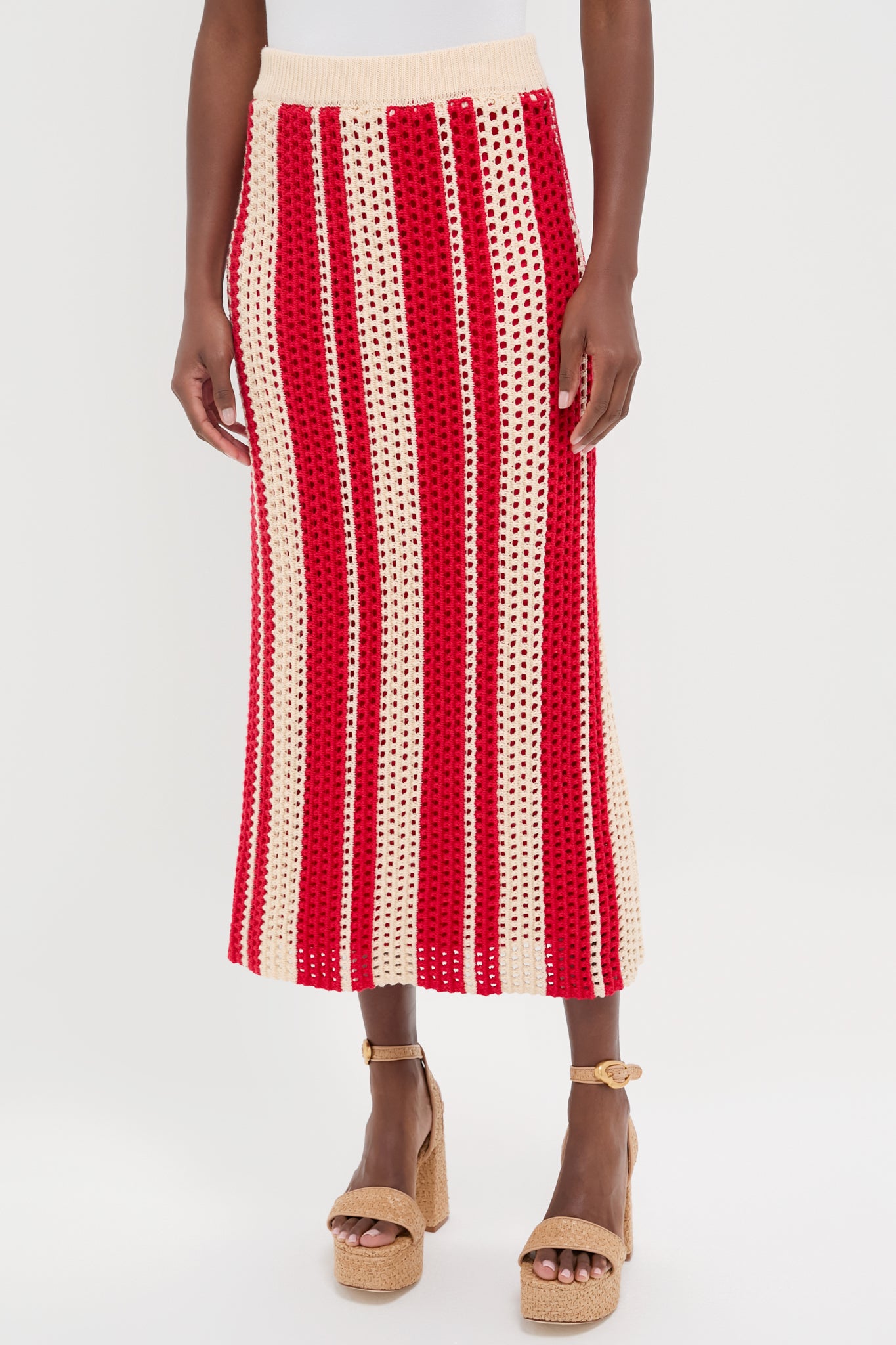 A woman wears a beige and red crochet midi skirt with vertical striped design, styled with tan platform sandals.