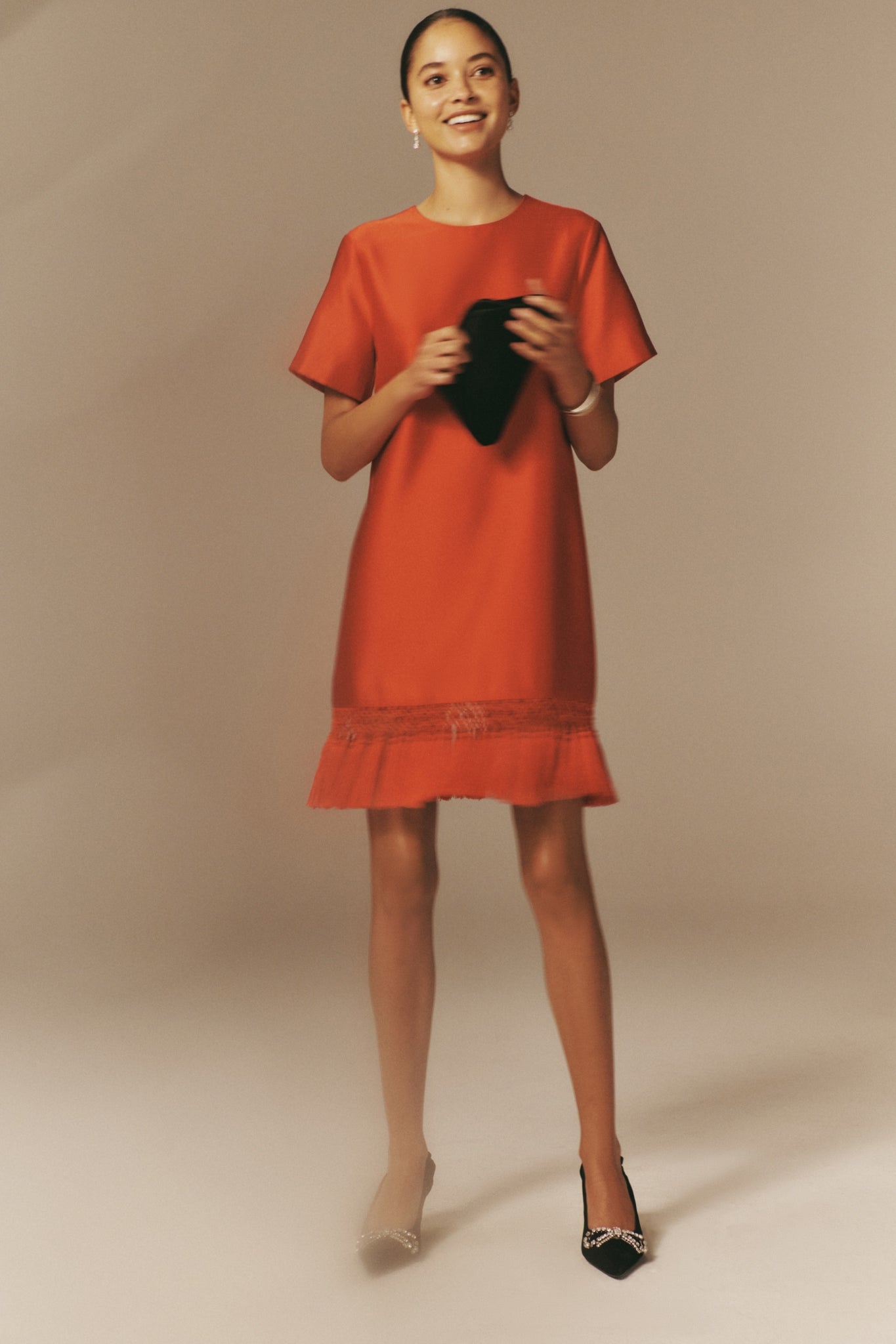 Young woman in a Red Dupioni Tassel Downing Dress with a classic silhouette and fun fringe hem, paired with high-end black heels and a clutch for an effortless festive look.