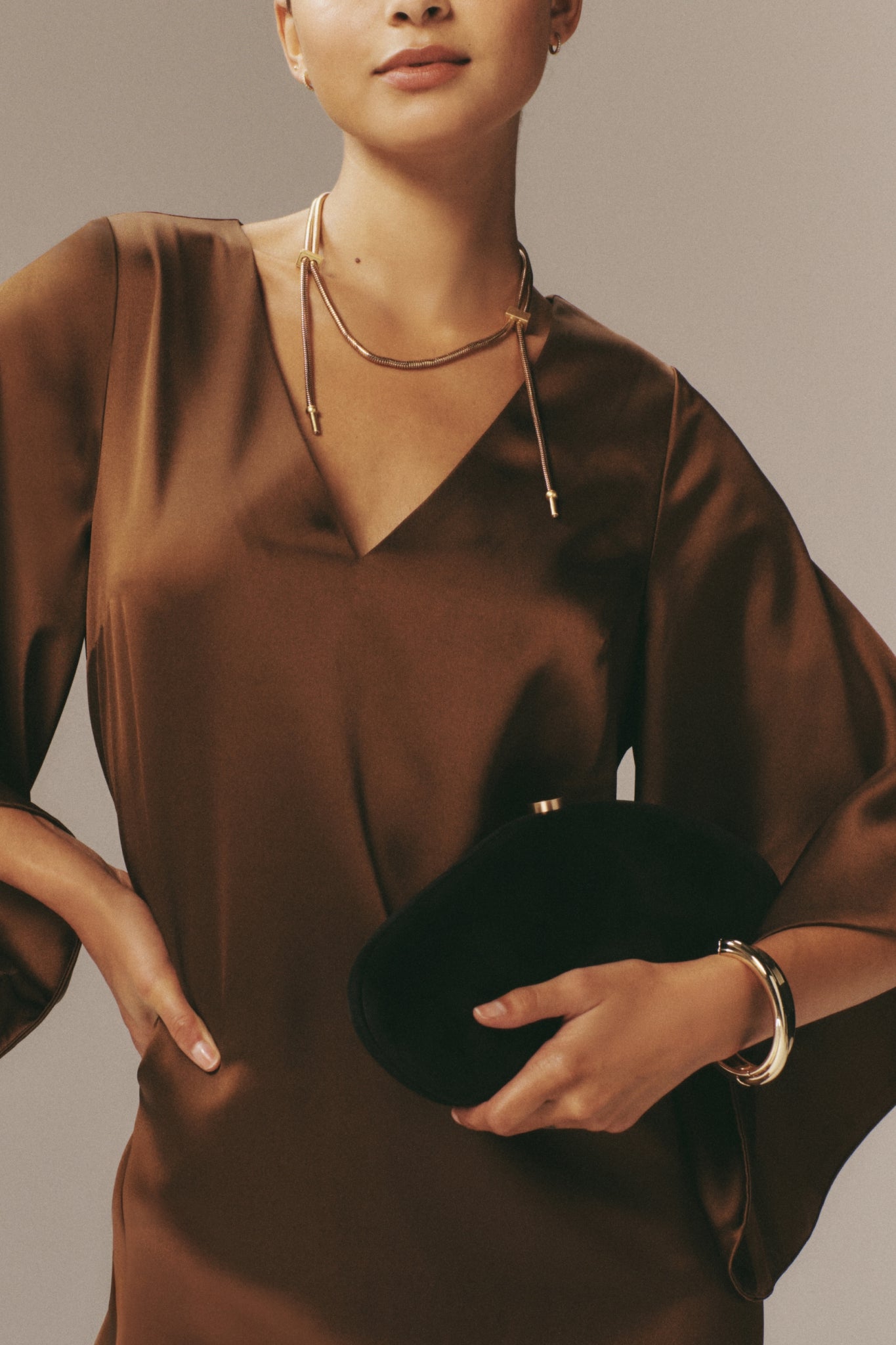 Woman holds the Black Caldera Bag, a classic, high-end velvet clutch with sculptural details and gold clasp, exemplifying effortless elegance and fun sophistication.