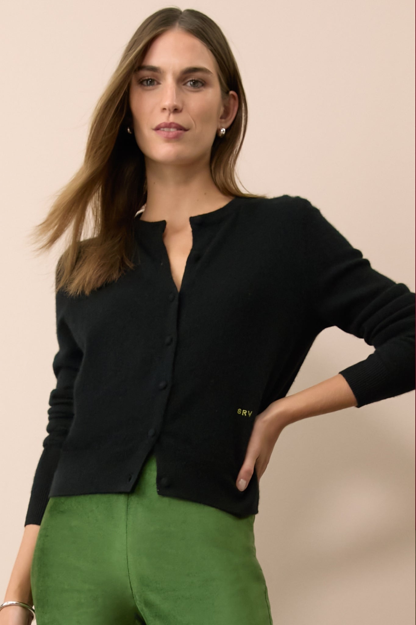 Woman in a black cashmere cardigan with the letters SRV monogrammed in green. 