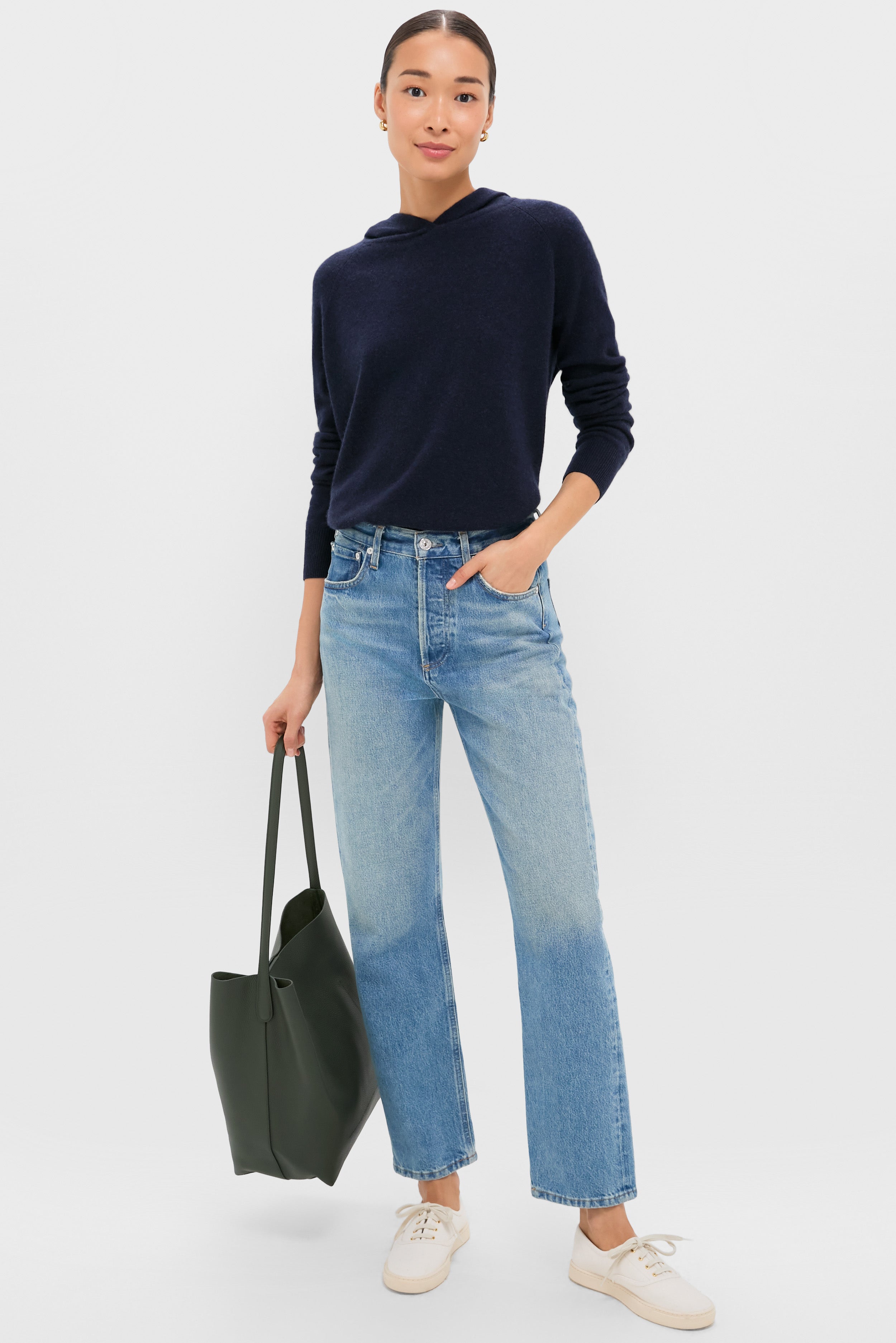 A person faces forward, wearing a Metrobazaarstore navy hoodie, light blue straight-leg jeans, white sneakers, and carrying a large dark green tote bag.