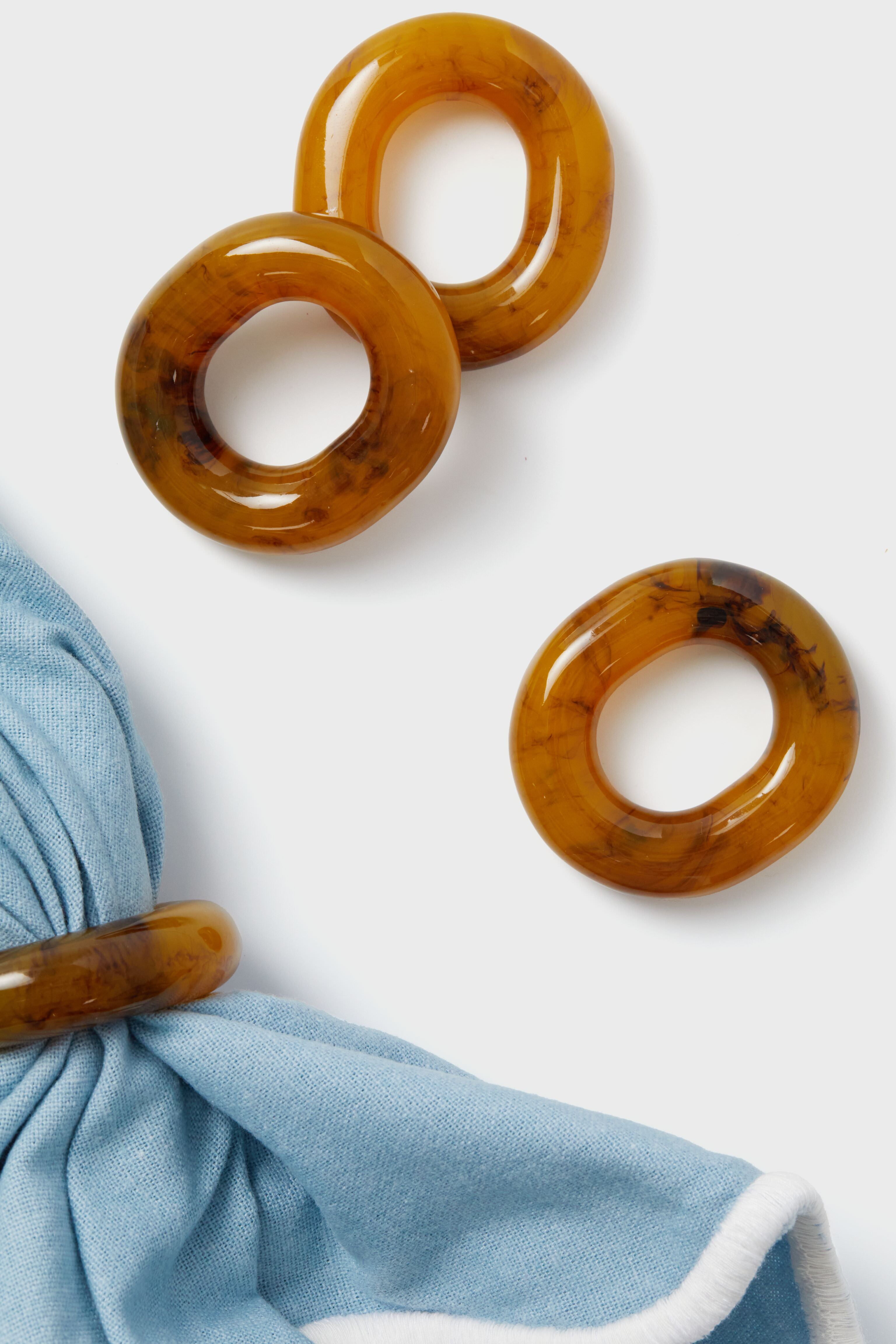 Four oval-shaped amber Tortoise Catena Link Napkin Rings by Metrobazaarstore Home, one displaying light blue fabric, are arranged on a white surface—ideal as hostess gifts or for entertaining.