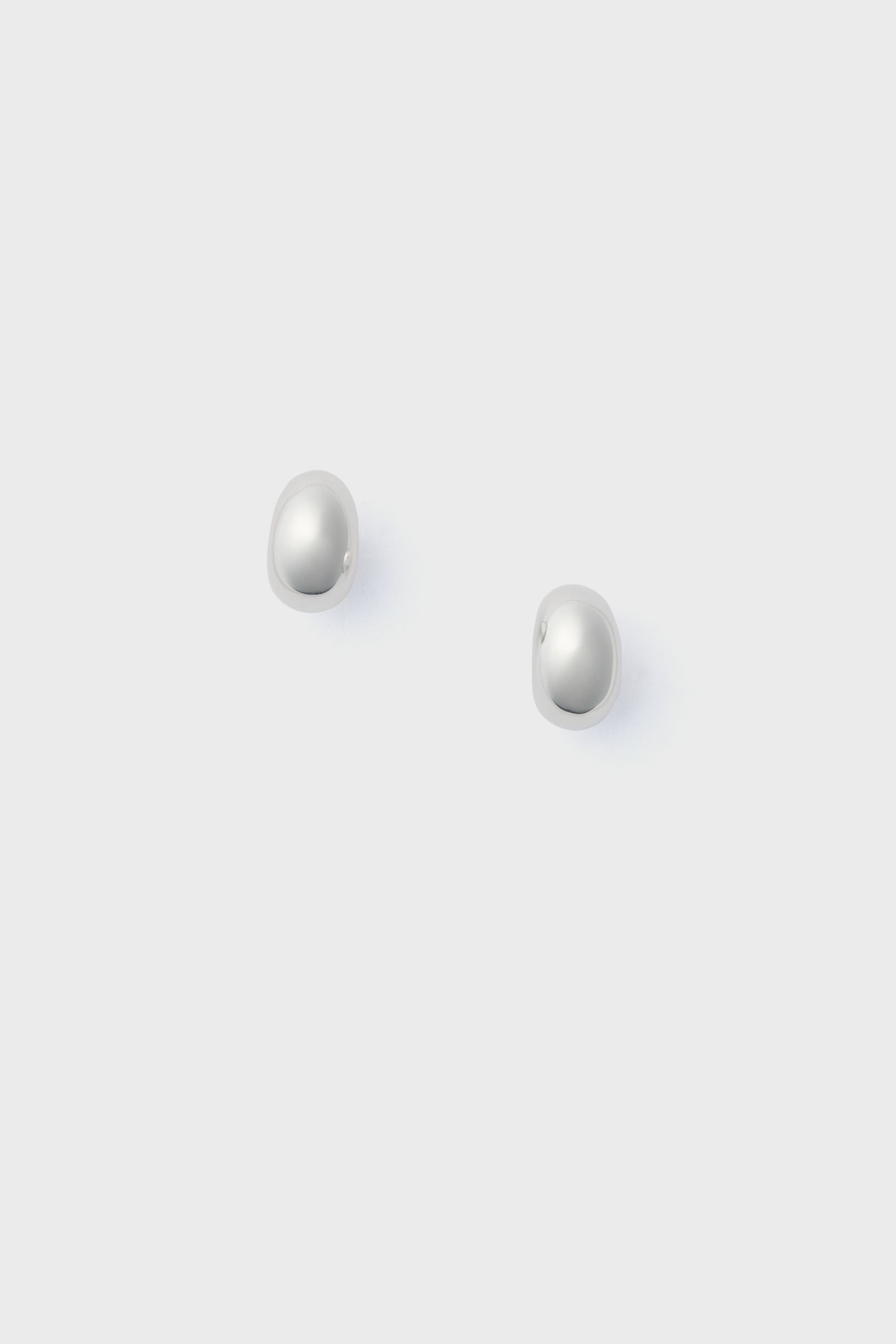 A pair of small, round, white pearl stud earrings by Lie Studio is displayed on a simple light grey background.
