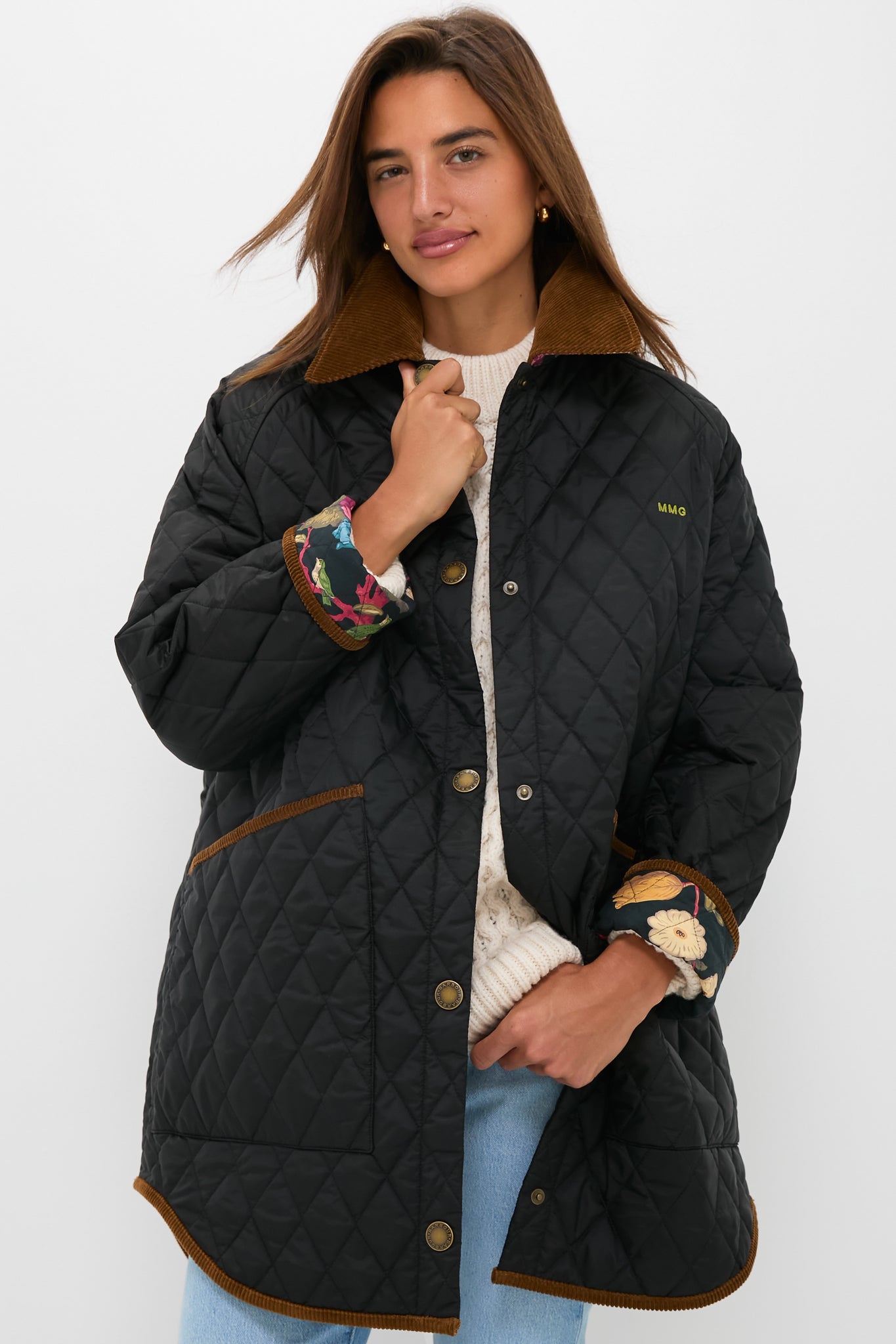 A woman stands against a plain background wearing the Barbour x Metrobazaarstore Miley quilt jacket with diamond stitching, brown trim, and a corduroy collar over a cream sweater and blue jeans.