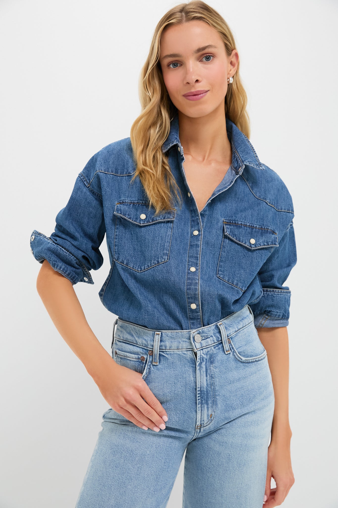A woman wears an Alex Mill vintage denim shirt with rolled-up sleeves and high-waisted light blue jeans, showcasing classic essentials.