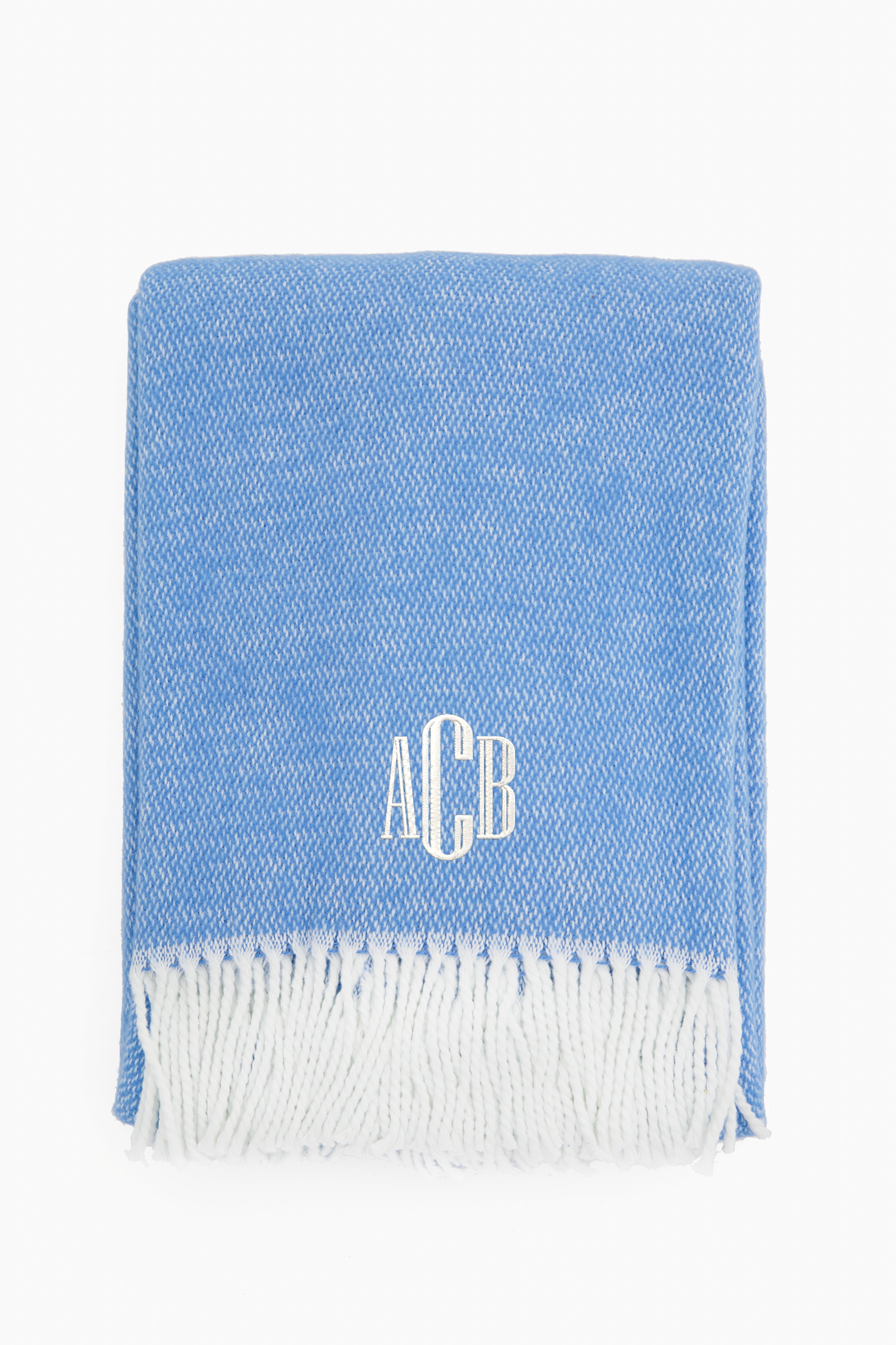 A folded blue Matouk cotton throw blanket with white fringe and white ACB monogram embroidered on the front. Ideal for those seeking high-quality linens.