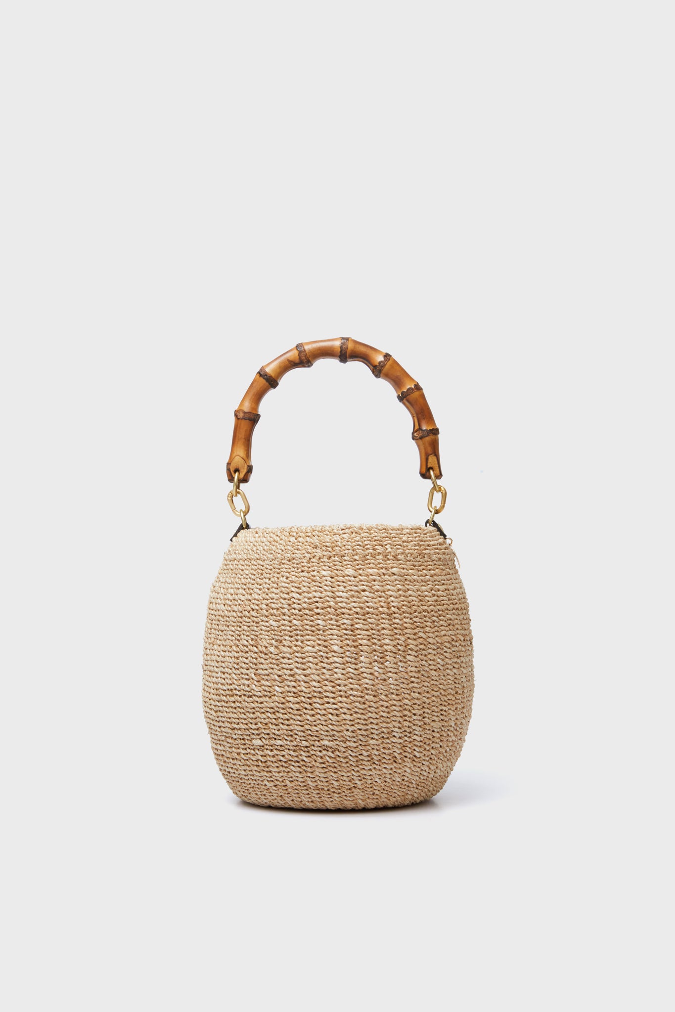 The Clare V round woven straw handbag, inspired by the Cream Pot de Miel Bag and featuring a curved bamboo handle, is elegantly showcased.