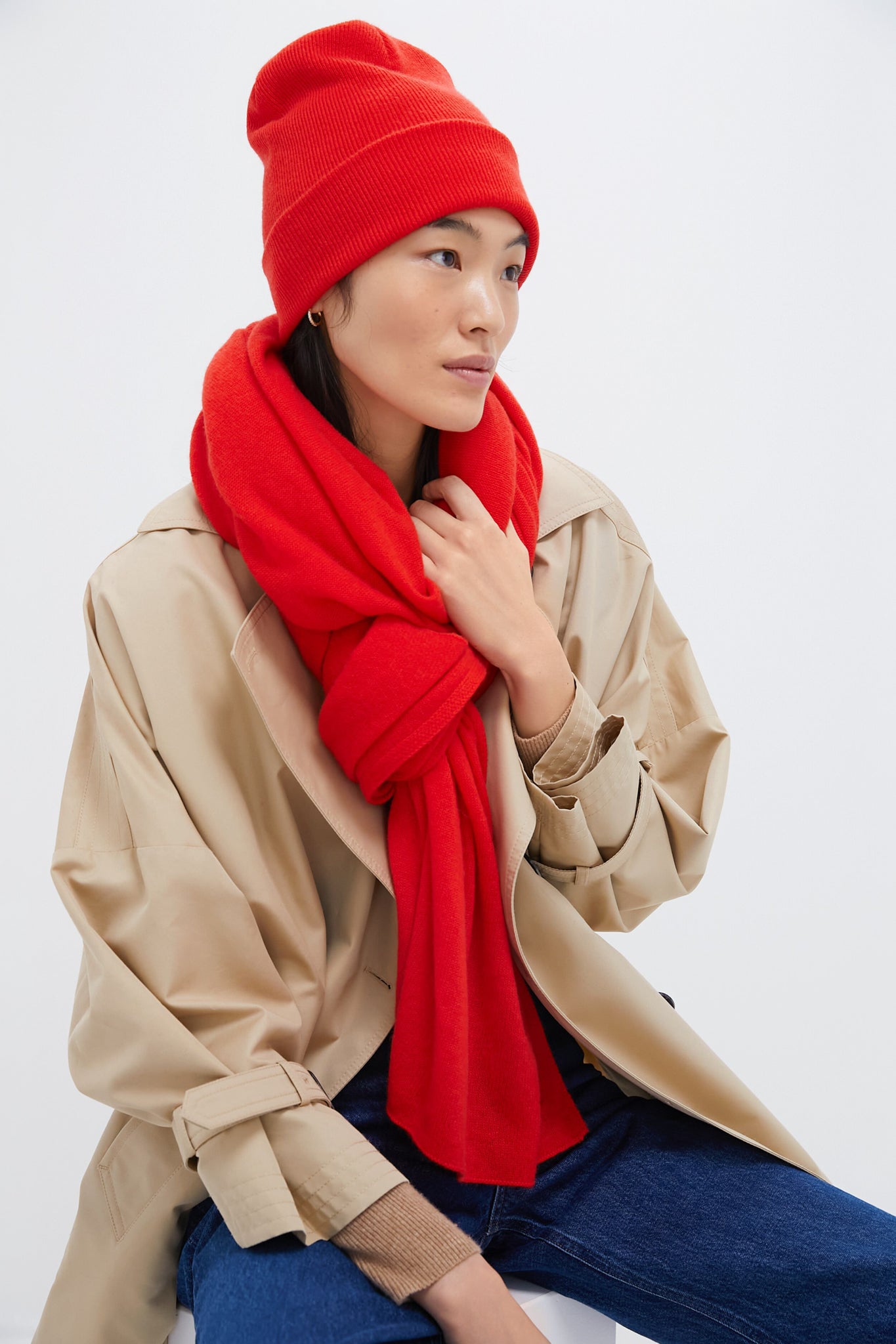 Dressed in a Metrobazaarstore red beanie, cashmere scarf, beige trench coat, and blue jeans against a white background—an effortlessly stylish look that makes the perfect holiday gift.