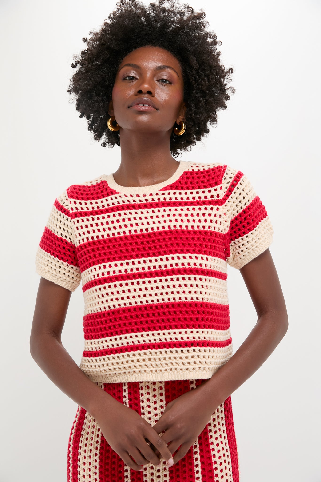 Person in a Hyacinth House short-sleeved knit top with burnt red and beige stripes, paired with the matching skirt, standing against a plain light background.