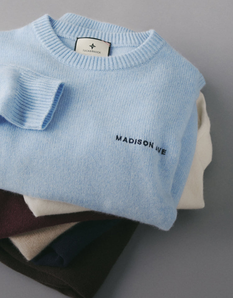 Pile of cashmere sweaters. Top sweater is blue with a monogram that says "Madison Ave" 