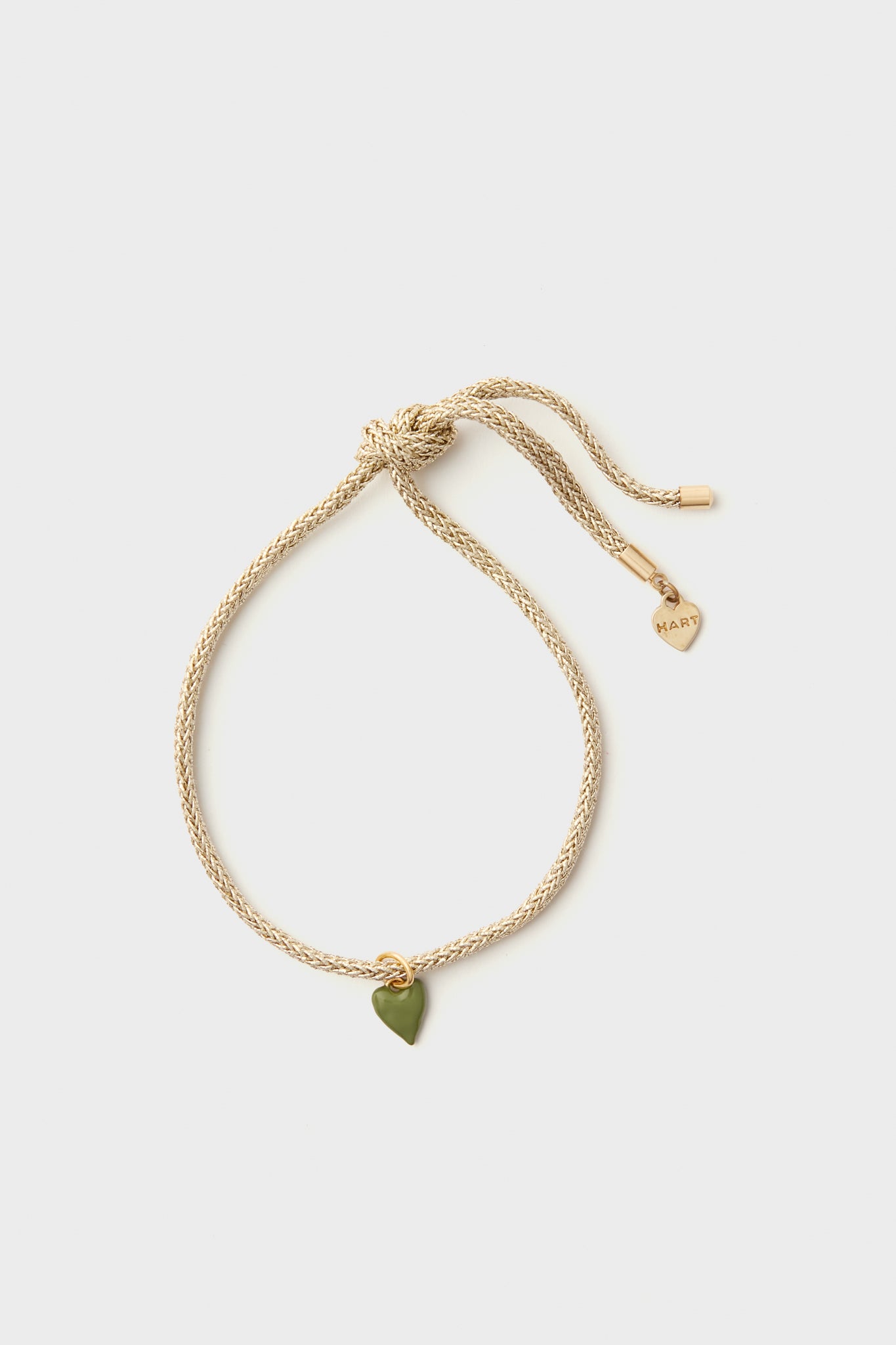 An adjustable Gold Lurex Cord Bracelet by HART, featuring a green enamel heart charm and a gold heart tag engraved with MARLY.