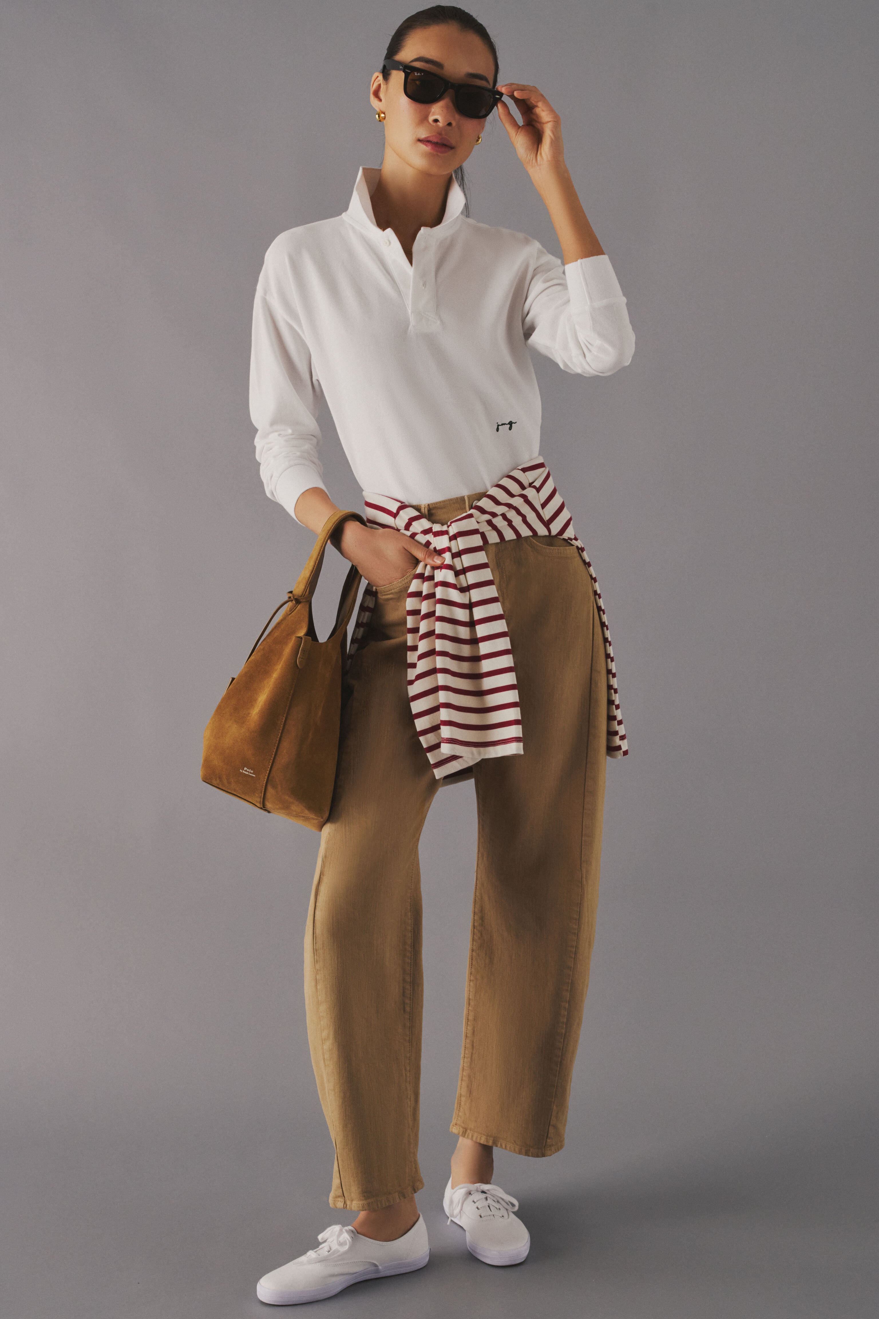 Woman standing in a studio in a white long sleeve polo with monogrammed initials on the waist. 