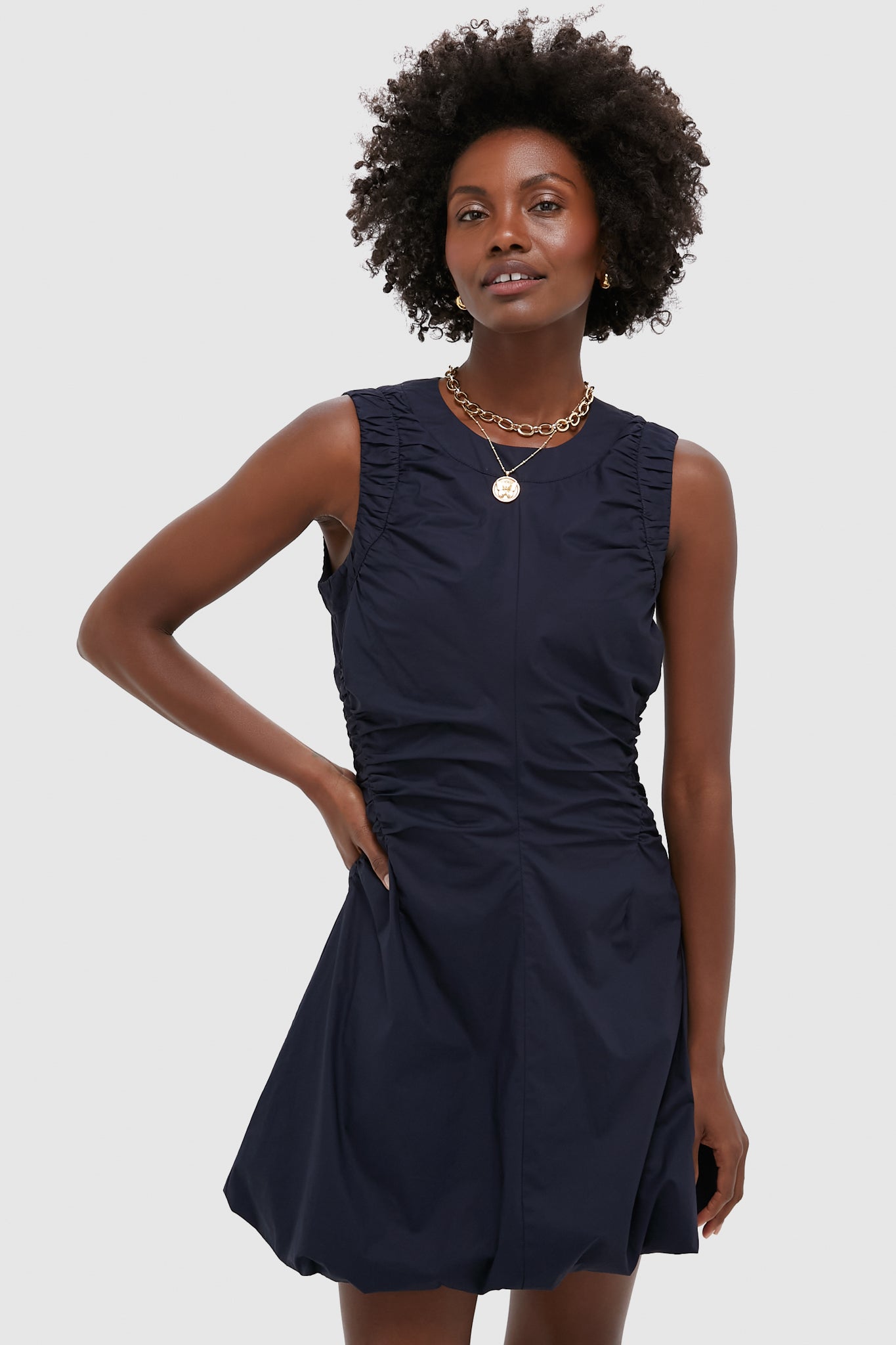 A woman wears a Metrobazaarstore sleeveless navy blue ruched dress with gathered sides and a flared skirt, styled with layered gold necklaces—ideal for cocktail hours.