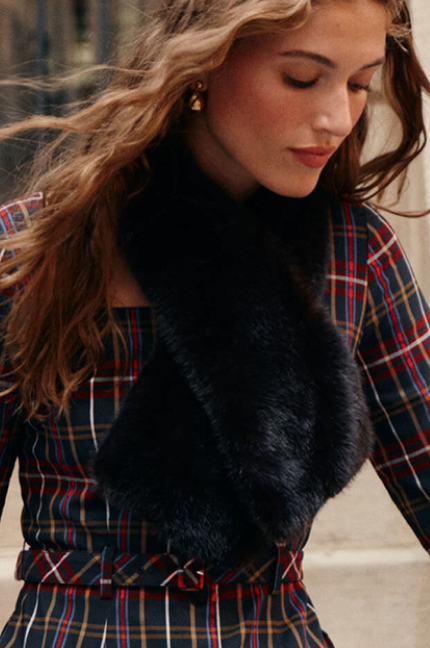 A woman wearing a tartan patterned mini dress and a brown fur scarf.