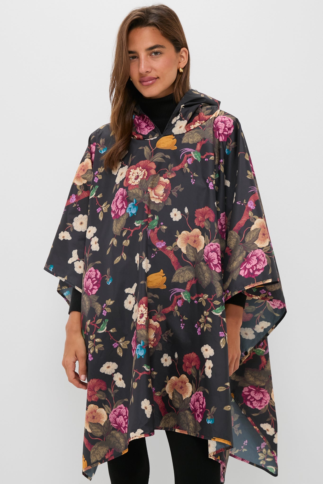 Someone wears a Barbour x Metrobazaarstore dark, packable floral poncho with a hood, standing against a plain light background.