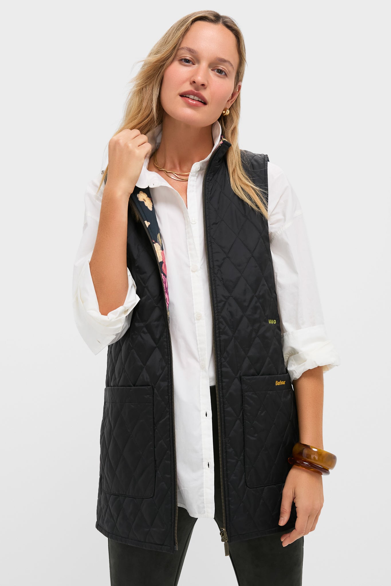 A woman wears a white button-up shirt and a Barbour x Metrobazaarstore black quilted vest with front pockets and a reversible Paisley liner, posing against a plain light background.